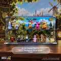 A two-tier clear acrylic display case for LEGO minifigures, shown holding multiple colorful LEGO Shrek character figures against a printed fantasy forest backdrop. The case sits on a wooden surface with a themed LEGO Brick Land set background.