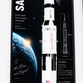 A framed educational poster featuring a detailed LEGO-style Saturn V rocket, Earth, and space graphics with text reading 'Explore. Discover.