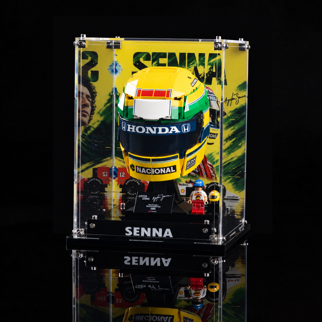 Acrylic display case featuring a LEGO Ayrton Senna helmet from 1988, mounted on a black base with printed race graphics and signatures. The product is shown against a yellow and green graphic background with 'Happy Brick Land' branding and text specifying the LEGO model is not included.